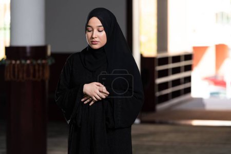 Téléchargez les photos : Une belle femme musulmane en robe noire avec hijab priant dans une mosquée. - en image libre de droit