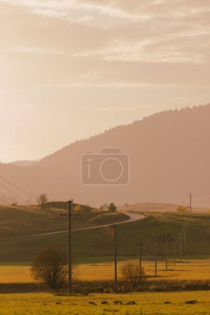 Téléchargez les photos : Une verticale de champs avec des lignes électriques et des stations autour, montagnes brumeuses et ciel en arrière-plan - en image libre de droit