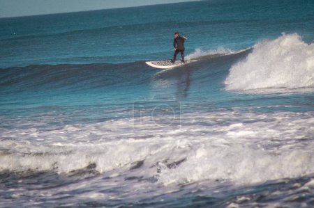 Foto de Una escena de un hombre remando en el mar de pie sobre la pizarra blanca sobre las olas durante el día - Imagen libre de derechos
