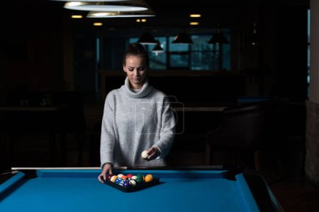 Photo for A young woman standing at the pool table arranging billiard balls in a triangle. - Royalty Free Image