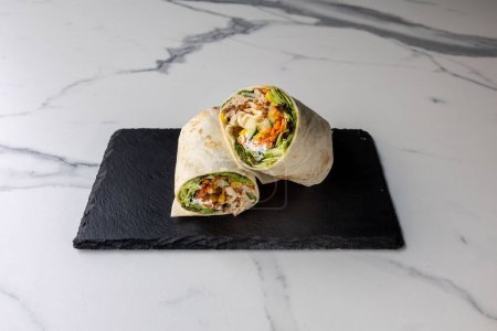 Photo for A delicious chicken wrap served on a black board on the marble table - Royalty Free Image