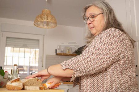 Téléchargez les photos : Femme aux cheveux blancs coupant des tranches de pain maison fraîchement cuit - en image libre de droit