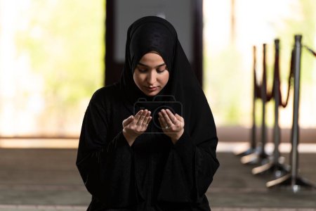 Foto de Una hermosa mujer musulmana vestida de negro con hiyab rezando en una mezquita. - Imagen libre de derechos