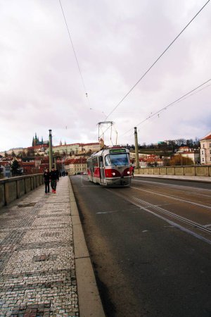Photo for A vertical shot of the people walking along the Manes Bridge in Prague, Czech Republic with the tram passing by in the afternoon - Royalty Free Image