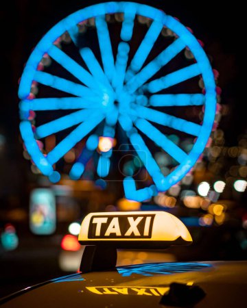 Photo for A vertical night shot of a taxi sign in front of an illuminated ferris wheel in downtown Cologne, Germany - Royalty Free Image