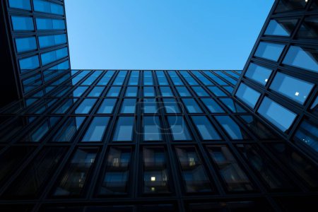 Foto de Una toma de ángulo bajo del moderno edificio de oficinas de vidrio contra un cielo azul oscuro - Imagen libre de derechos
