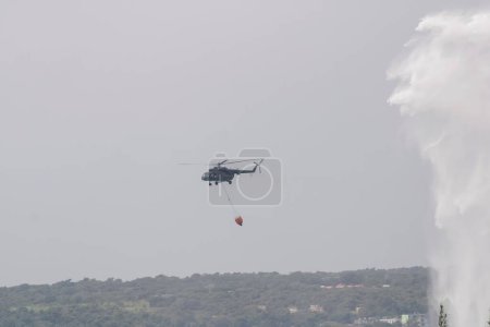 Photo for The Cuban armed forces helicopter putting out the fire from the explosion of the oil tanks of the supertanker with Bambi buckets in Matanzas Cuba - Royalty Free Image