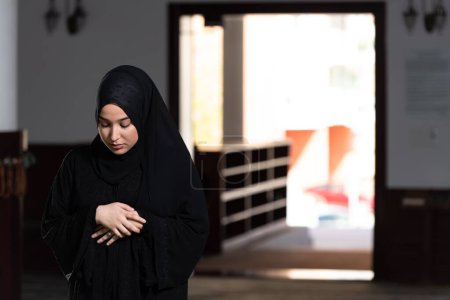 Foto de Una hermosa mujer musulmana vestida de negro con hiyab rezando en una mezquita. - Imagen libre de derechos