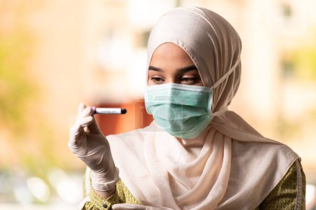 Photo for A Medical Doctor Nurse Muslim Woman Wearing Protective Mask and Gloves - Holding Virus Blood Test - Royalty Free Image