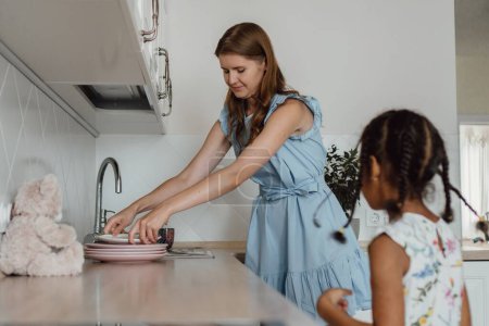 Téléchargez les photos : La mère et la fille hispaniques lavant la vaisselle dans la cuisine - en image libre de droit