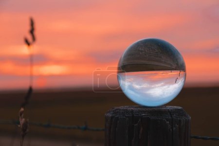 Téléchargez les photos : Une boule de verre sur poteau en bois sur fond flou dans un champ au coucher du soleil - en image libre de droit
