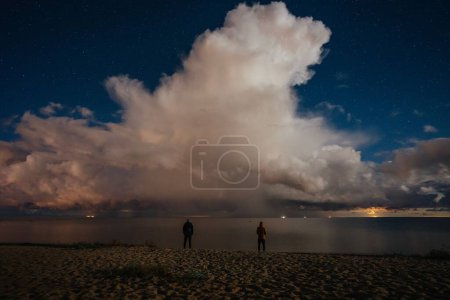 Téléchargez les photos : Longue exposition d'un lac et de deux personnes debout sur le rivage devant les nuages et le ciel - en image libre de droit