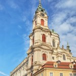 A vertical low angle shot of the historic St. Nicholas Church against a bright blue sky in Prague