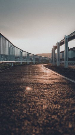 Foto de Un plano vertical a nivel del suelo de una carretera asfaltada con una valla metálica cerca de ella - Imagen libre de derechos