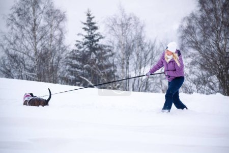 Foto de Mujer con perro afuera jugando en la nieve - Imagen libre de derechos