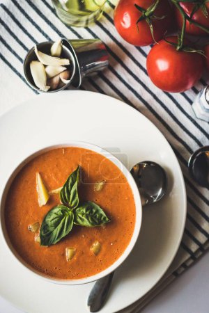 Photo for A vertical top view of a tomato soup decorated with basil leaves in a round white bowl - Royalty Free Image