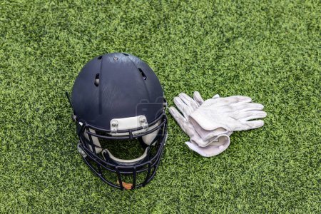 Téléchargez les photos : Un casque de football américain et une paire de gants blancs posés sur l'herbe - en image libre de droit