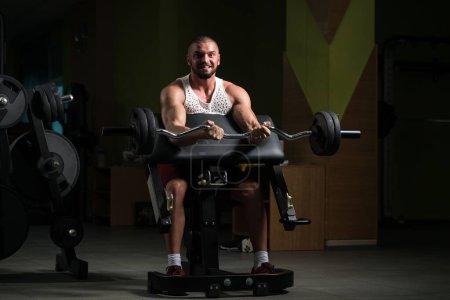 Téléchargez les photos : Un homme musclé faisant l'exercice lourd de poids pour des biceps avec Barbell dans le gymnase - en image libre de droit