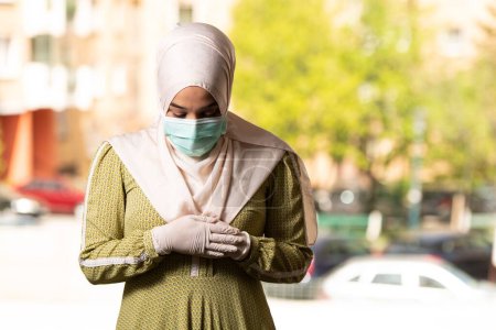 Foto de Una joven musulmana rezando al aire libre usando máscara protectora y guantes - Imagen libre de derechos