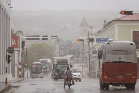 Téléchargez les photos : Une route avec des voitures et des vélos lors de fortes pluies dans la ville de Matanzas, Cuba - en image libre de droit