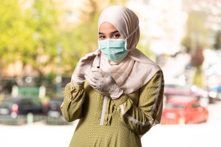 Téléchargez les photos : Une infirmière médecin musulmane portant un masque protecteur et des gants - Tenir un test sanguin de virus - en image libre de droit