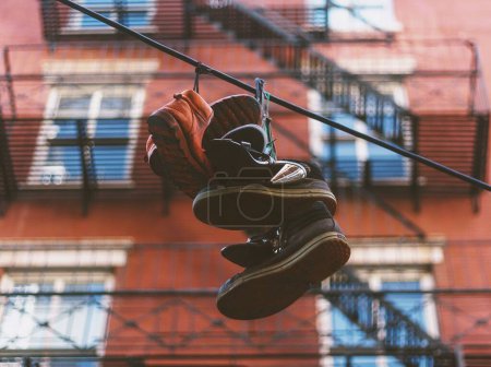 Photo for A selective focus shot of a few pairs of shoes hanging to dry outdoors with building in background - Royalty Free Image