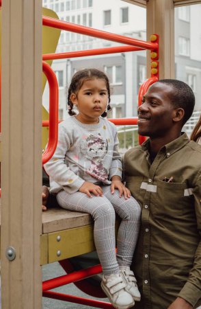 Téléchargez les photos : Un père noir heureux avec sa petite fille sur une aire de jeux - en image libre de droit