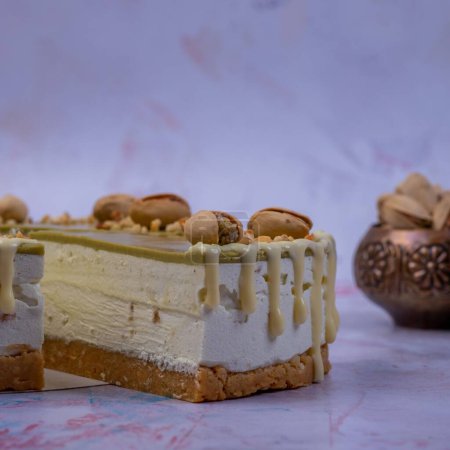 Téléchargez les photos : Un gros plan du morceau d'un gâteau au fromage à la crème aux pistaches décoré de pistaches et de crème vanille sur un fond flou - en image libre de droit