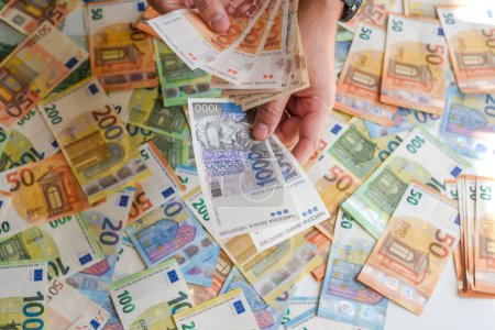 Téléchargez les photos : Une main humaine tenant les billets en kuna croate sur fond de billets en euros - en image libre de droit