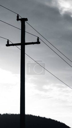 Téléchargez les photos : Une échelle de gris de champs avec des lignes électriques et des stations autour, montagnes et fond de ciel ensoleillé - en image libre de droit