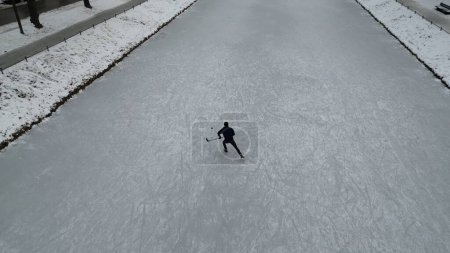 Téléchargez les photos : Un homme en tenue noire tenant un bâton de hockey et patinant sur une patinoire, par une journée d'hiver glacée - en image libre de droit
