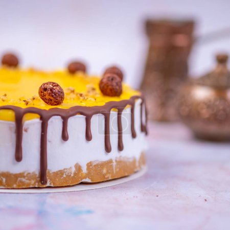 Téléchargez les photos : Un gros plan du gâteau au fromage avec une surface jaune décorée de crème au chocolat et de boules de chocolat sur un fond flou - en image libre de droit
