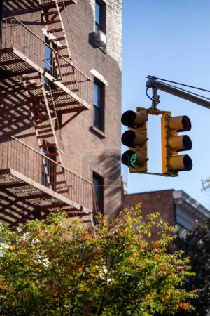 Photo for A vertical shot of hanging traffic lights and a fire escape staircase of a brick building in New York. - Royalty Free Image