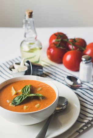 Foto de Una toma vertical de sopa de tomate con hojas de albahaca e ingredientes en el fondo - Imagen libre de derechos