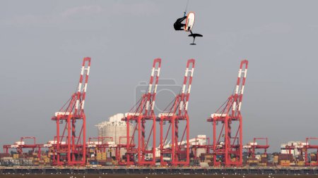 Téléchargez les photos : Un Kiteboarder planant avec des grues rouges en arrière-plan. New Brighton, Merseyside, Angleterre. - en image libre de droit