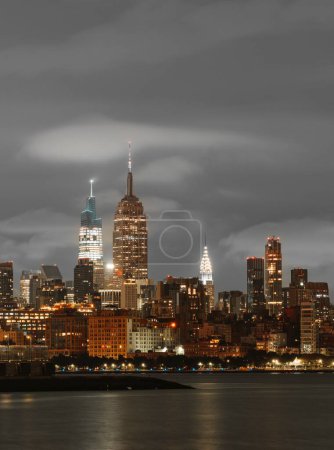Foto de Una vertical del Empire State Building contra el mar iluminada por las luces de la ciudad de Nueva York en un día nublado - Imagen libre de derechos