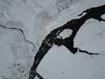 Téléchargez les photos : Vue aérienne d'un ruisseau glacé traversant un champ blanc enneigé en Islande - en image libre de droit