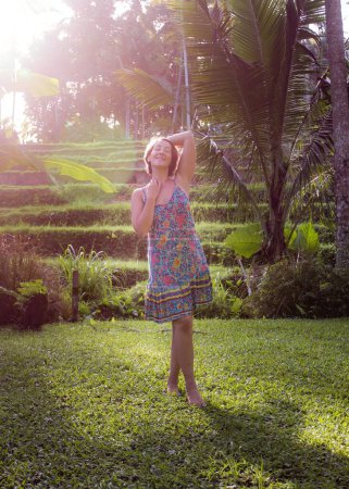 Photo for A vertical shot of a young woman in a summer dress enjoying the morning light in a tropical garden. - Royalty Free Image