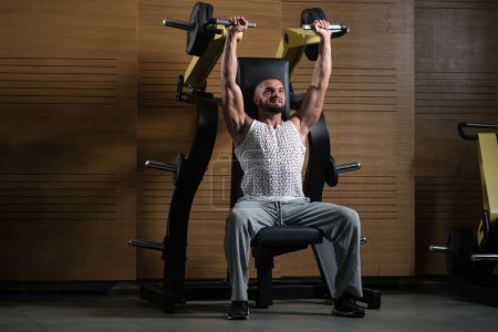 Téléchargez les photos : Un beau bodybuilder musculaire faisant l'exercice lourd de poids pour des épaules dans le gymnase - en image libre de droit