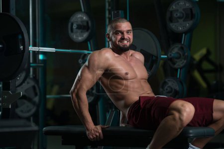 Foto de Un guapo sonriente caucásico atractivo joven hombre con musculoso cuerpo ejercitando en gimnasio - Imagen libre de derechos
