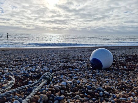 Photo for A white boat buoy on the beach with small stones in front of the wavy sea in Bexhill-on-Sea, England - Royalty Free Image