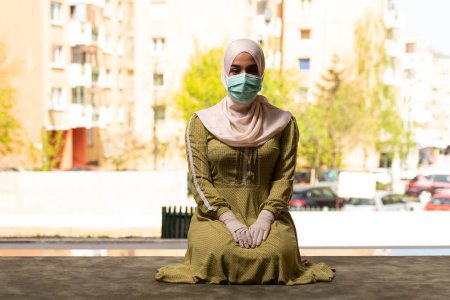 Téléchargez les photos : Une jeune femme musulmane priant à l'extérieur portant un masque protecteur et des gants - en image libre de droit