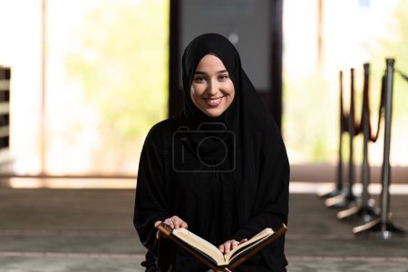 Foto de Una hermosa mujer musulmana en una mezquita leyendo el Corán. Fe musulmana, cultura. - Imagen libre de derechos