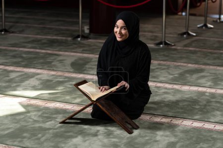 Photo for A beautiful Muslim woman in a mosque reading Quran. Muslim faith, culture. - Royalty Free Image