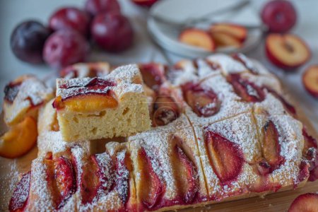Téléchargez les photos : Gros plan d'un gâteau aux prunes avec de la poudre de sucre sur une planche à découper en bois - en image libre de droit