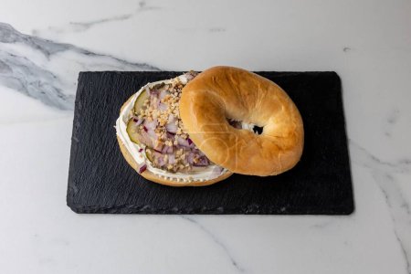 Foto de Un delicioso bagel con cebollas servido en la pizarra negra sobre la mesa de mármol - Imagen libre de derechos