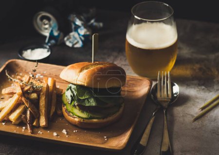 Téléchargez les photos : Un gros plan d'une assiette en bois avec un hamburger et des frites, des canettes de bière en arrière-plan - en image libre de droit