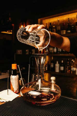 Foto de Una vertical de un barman haciendo cóctel en el gran frasco de vidrio con bebidas alcohólicas en el suelo - Imagen libre de derechos