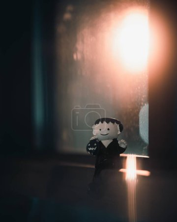 Photo for A vertical shot of a small Halloween Frankenstein figurine put on the ledge of a window with light in the background - Royalty Free Image