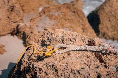 Téléchargez les photos : Plan rapproché d'une ligne de fil placée sur une roche brune sur le rivage d'une plage - en image libre de droit